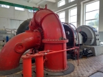 Große rote Turbine in einer Werkstatt mit gebogenen Rohren und Zylindern auf einem grauen Betonboden mit rot-weißem Schachbrettmuster